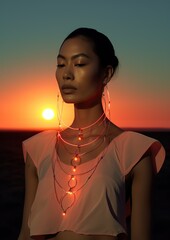 A surreal goddess stands in a romantic sunset, her futuristic clothing and glittering sun-inspired necklace and earrings glowing against the sky