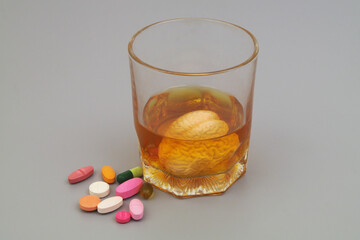 Alcohol and health concept. Glass with drink and human brain and drugs on gray background.