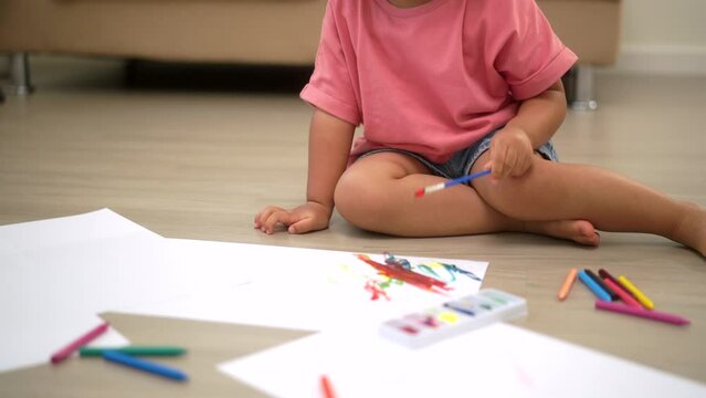 Little cute girl creating and water color painting activity with paint brushes in living room at home. Kids activity. Child physical, Emotional, Cognitive development concept.