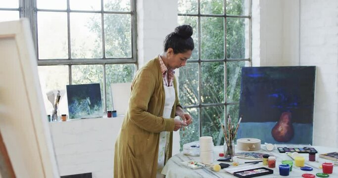 Biracial female artist preparing paints in studio, slow motion