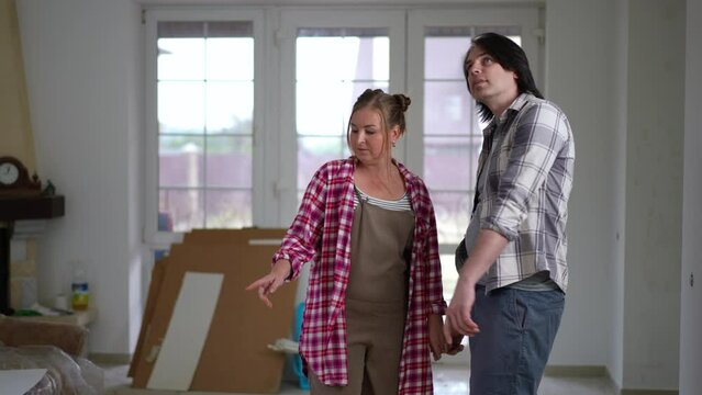 Plus-size Caucasian man and woman standing in new house looking around talking in slow motion smiling. Live camera zoom in to happy loving couple. DIY concept