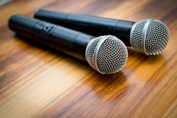 Two radio microphones lying on a wooden table surface.