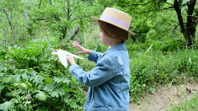 A 9-year-old girl in a hat launches a paper bird into the air in nature.