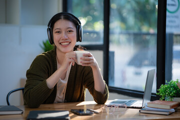 Young beautiful Asian businesswoman holding a coffee cup while sitting in her office room.