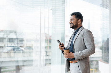 Fototapeta premium A successful Indian-Asian male CEO in a formal business suit is looking out the building
