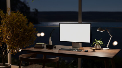 A modern dark home workspace at night with a computer on a table against the glass window
