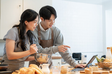 A lovely Asian couple is reading a pastry recipe on a tablet, enjoying cooking dates at home