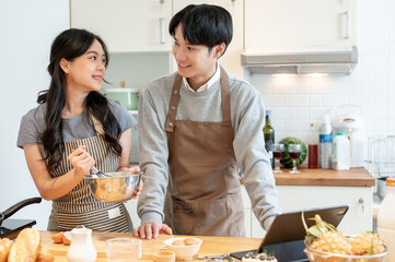 A beautiful Asian girlfriend is making pancakes in the kitchen with her boyfriend