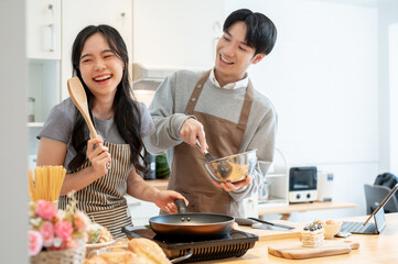 A joyful Asian couple is laughing, enjoying baking pastry, or making pancakes in the kitchen