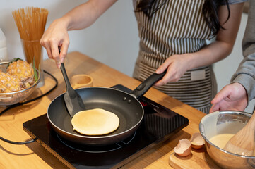 Close-up image of a female making pancakes in the kitchen with her boyfriend