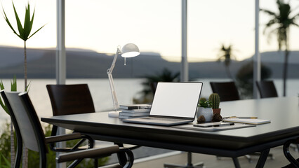 A laptop on a meeting table in a modern meeting room with large glass window with a nature view.