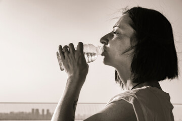 Portrait young dark-haired woman with bottle of water. Lady drinking water from plastic bottle quenching thirst after exercise