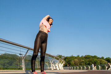 Young woman stretching back on footbridge on sunny day. Yoga practice and healthy lifestyle against of green plants and blue sky low angle shot