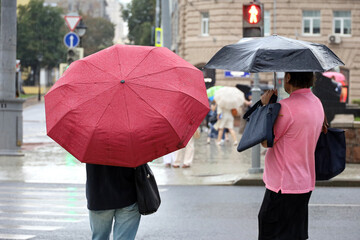 People with umbrellas standing on pedestrian crossing on red traffic light background. Rainy weather in city