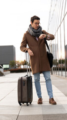 young standing leaning on his suitcase looking at the time