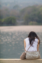 young woman sits on walkway by reservoir watching beautiful scenery of reservoir alone in the evening. back of woman sitting by reservoir alone in evening and with copy space for text.