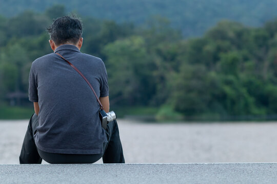 A depressed young man sat by the reservoir alone with a depressed feeling. The young man sat by the reservoir, depressed and staring into the water with emotional strain. Copy Space for text.