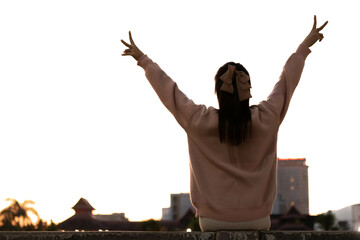 silhouette of young woman raising her hands above her head and making hand sign with two raised...