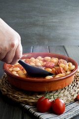 woman's hand picking up a spoonful of beans stewed in an earthenware dish