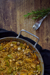 paella valenciana on cloth, with a fork and a sprig of rosemary on a wooden table, vertical.