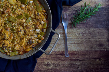 paella valenciana on cloth, with a fork and a sprig of rosemary on a wooden table, horizontal.