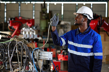 African electrician engineer or worker checking electric cable in robot factory