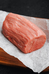 Fresh meat veal fillet on parchment and wooden board, dark background