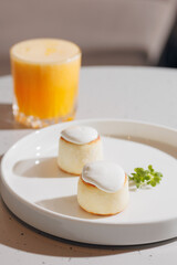 Closeup sweet syrniki, cottage cheese pancakes with white sauce, condensed milk. Healthy nutritious breakfast with orange juice