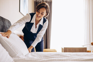 Woman housekeeper preparing bed cloths and pillows in the hotel room - obrazy, fototapety, plakaty