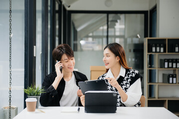 Two Asian businesswoman and man discuss investment project working and planning strategy with tablet laptop computer in office.