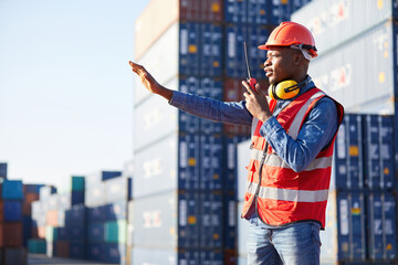 African factory worker or engineer using walkie talkie and showing stop gesture to crane car in containers warehouse storage - obrazy, fototapety, plakaty
