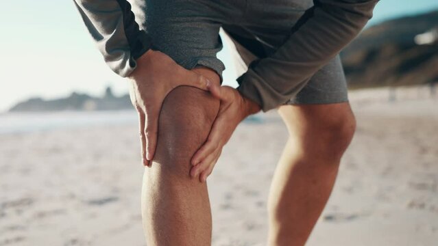 Knee pain, beach and legs of sports runner with health risk, exercise wound and emergency outdoor. Fitness man, ocean and closeup on hands of athlete with joint injury, first aid and workout accident
