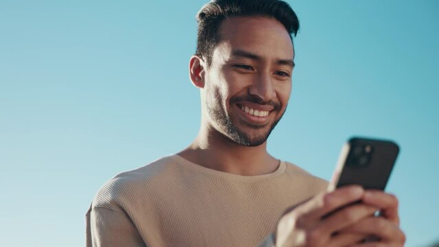 Blue sky, phone and young man typing a text message on social media, mobile app or website. Technology, online and happy Indian male person scroll on the internet with a cellphone for communication.