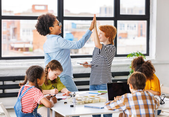 Teacher and joyful students celebrate   successful completion of collective school work in a bright classroom.