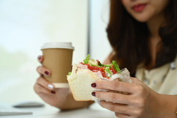 Woman hands holding delicious sandwich and paper cup coffee. Fast food and lifestyle concept