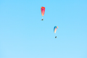 two colorful paragliders soaring through the blue sky