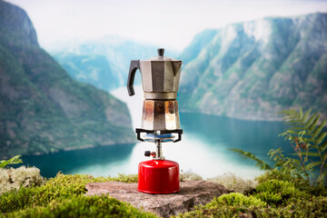 Cooking, making coffee or tea on a portable camping gas burner with a red gas cylinder with a Scandinavian nature background. Summer hiking, ecotourism, survival.