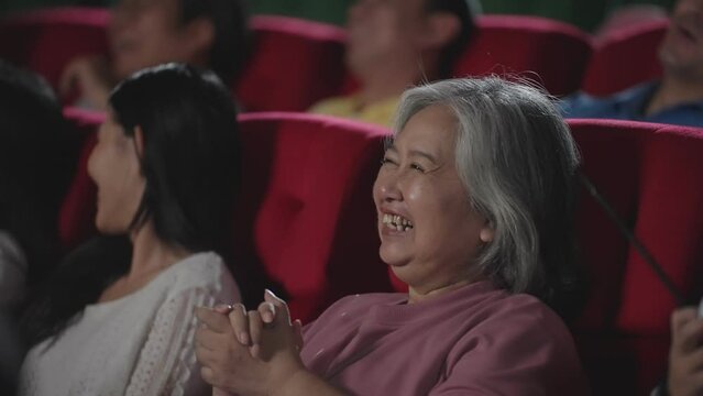 Close up portrait Asian woman laughing while watching comedy film in theater. Asian middle age woman watching comedy movie laughing while sitting on seat in movie theater