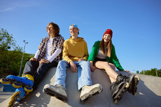 Joyful rollerskaters team of teenage people sitting on ramp