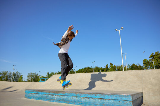 Young guy wearing inline skates doing balancing stunt at skateboard park