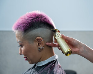 The hairdresser shaves the back of the head of a female client. Rear view of a woman with short pink hair in a barbershop.