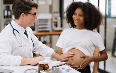 Obraz premium Happy pregnant woman has appointment with doctor at clinic. male medic specialist with stethoscope listens to baby's heartbeat in mother's belly. Pregnancy, health care concept.