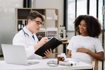 Fototapeta premium Happy pregnant woman has appointment with doctor at clinic. male medic specialist with stethoscope listens to baby's heartbeat in mother's belly. Pregnancy, health care concept.