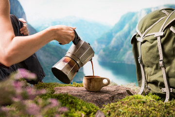 Woman tourist backpacker pouring coffee from a moka coffee maker into a traditional wooden Finnish cup Kuksa against the backdrop of a Scandinavian landscape