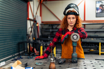 Portrait of adult woman standing indoors in metal workshop, looking at camera.