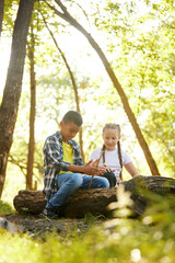 Children, boy and girl sitting on lo in forest on warm sunny day, playing, having fun, enjoying nature. Concept of leisure activity, childhood, summer, friendship, active lifestyle, fun, nature