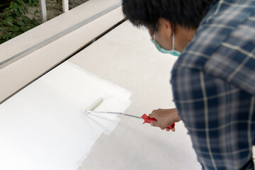 Painter man at work use a paint roller white color to wood board.