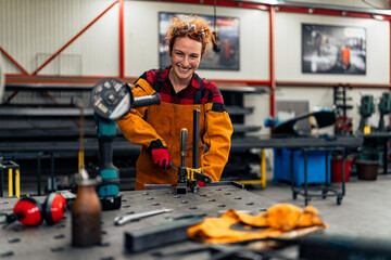 A young mechanical engineer works in the workshop and smiles at the camera, the owner of her business