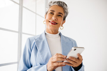 Empowered business woman in suit holding smartphone, deep in thought