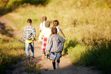 Happy and excited little boys and girls, children in casual clothes running on meadow, exploring nature on warm sunny day. Concept of leisure activity, childhood, summer, friendship, active lifestyle